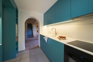 A kitchen with teal cabinets, a white countertop, and a stainless steel sink.