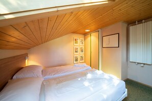 A bedroom with a wooden ceiling, a bed with white linens, and a wall with framed artwork.