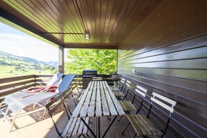 A covered outdoor area with a wooden table and benches, overlooking a scenic landscape.