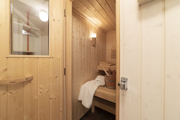 A wooden sauna room with a bench, a towel, and a bucket.