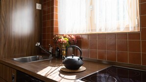 Cozinha com chaleira no balcão, pia e janela com cortinas.