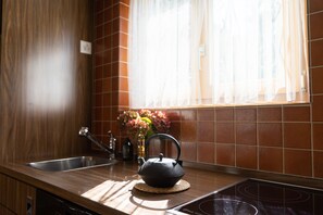 Una cocina con hervidor en la encimera, un lavabo y un ventanal con cortinas.
