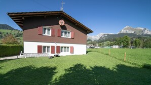 Uma casa de dois andares com telhado inclinado, antena parabólica e vista para montanhas ao fundo.
