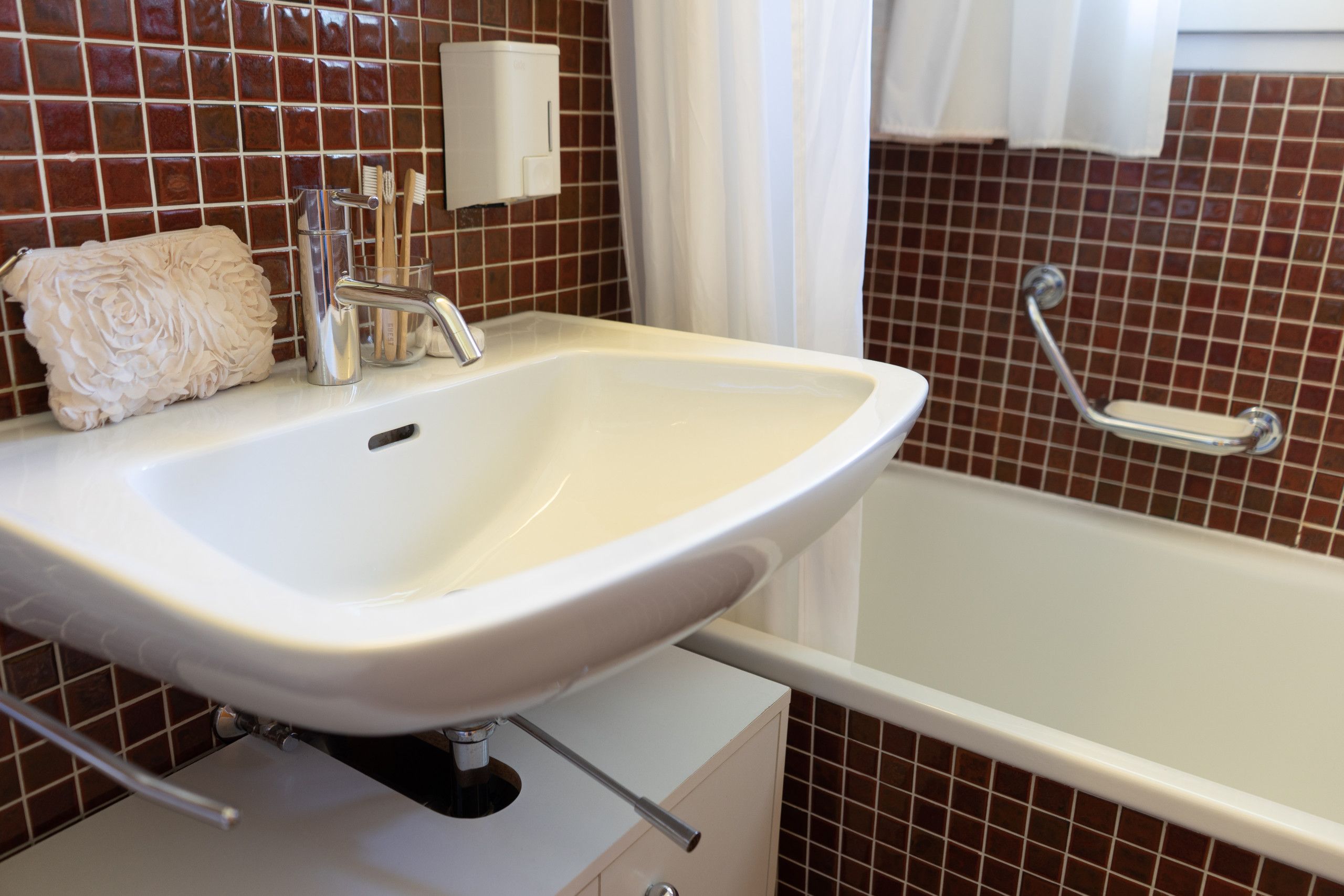 Un baño con lavamanos blanco, espejo, toalla y bañera.