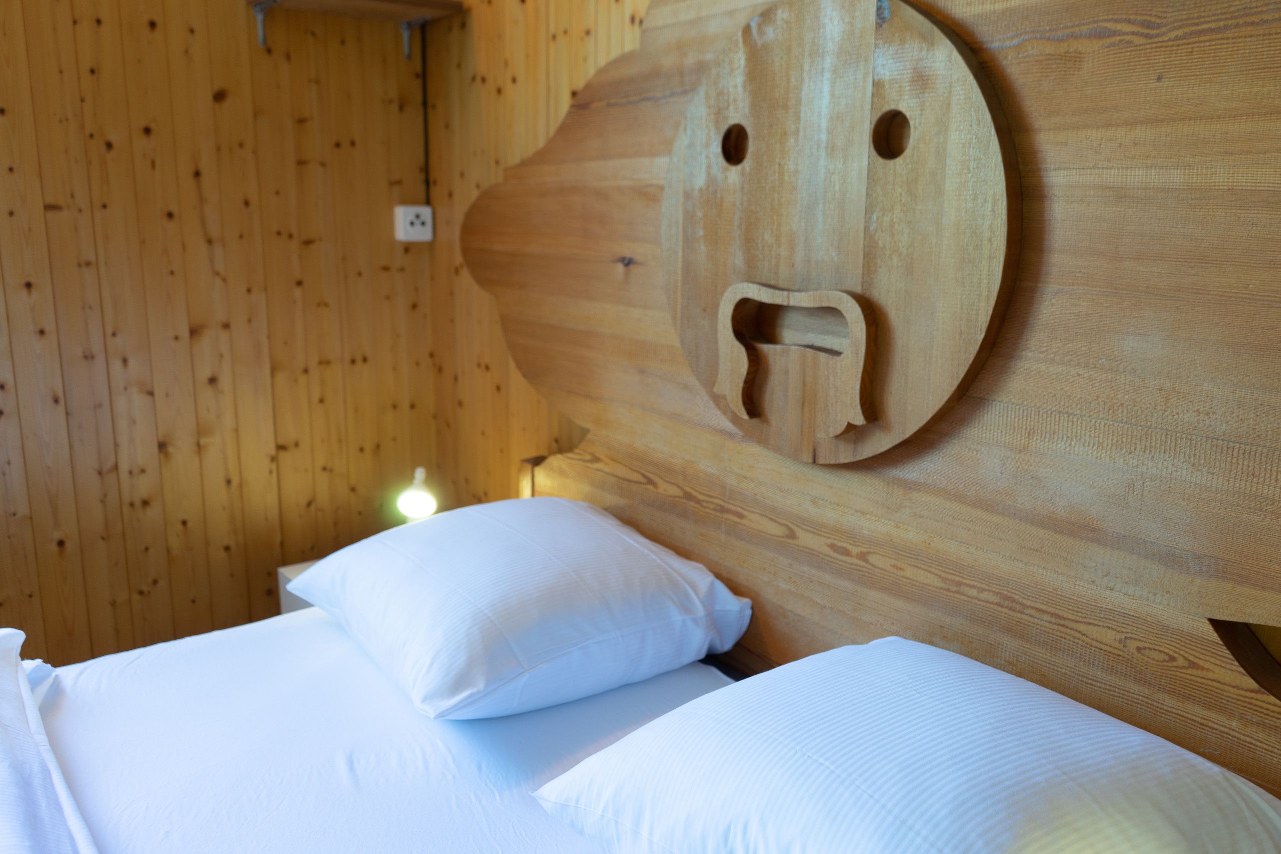 Una habitación de cabaña de madera con cama, almohadas y un original cabecero de madera con diseño que asemeja un rostro.