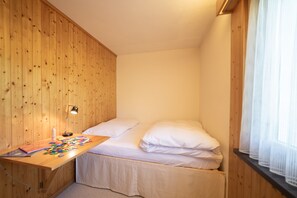 Pequeña habitación individual con paredes de madera y un escritorio con lámpara.