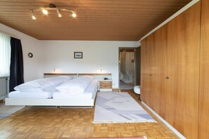 Un dormitorio con techo de madera, una cama con ropa de cama blanca, una mesita de noche con lámpara y un armario.