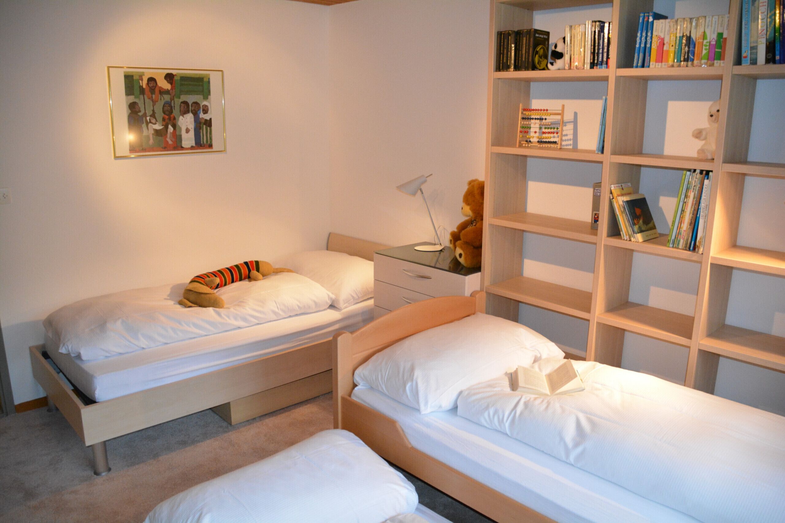Ein Schlafzimmer mit zwei Einzelbetten, einem Nachttisch mit Lampe, einem Bücherregal und einem gerahmten Bild an der Wand.
