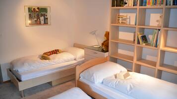 Ein Schlafzimmer mit zwei Einzelbetten, einem Nachttisch mit Lampe, einem Bücherregal und einem gerahmten Bild an der Wand.