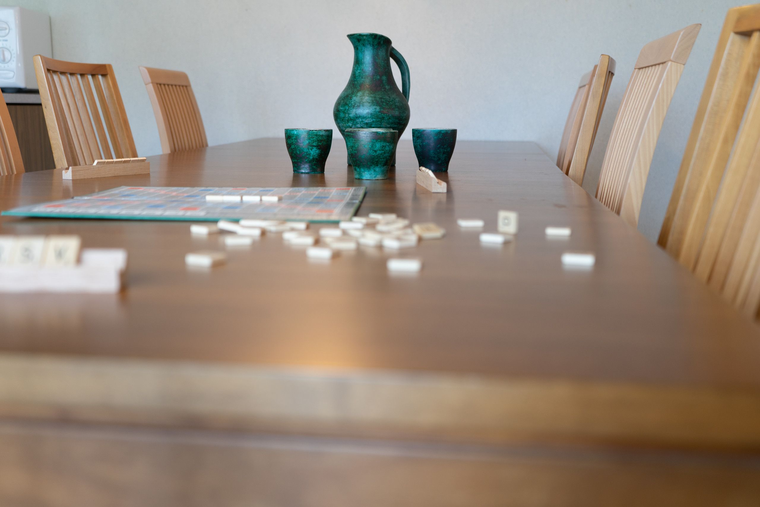 A wooden table with a board game, a green vase, and scattered game pieces.