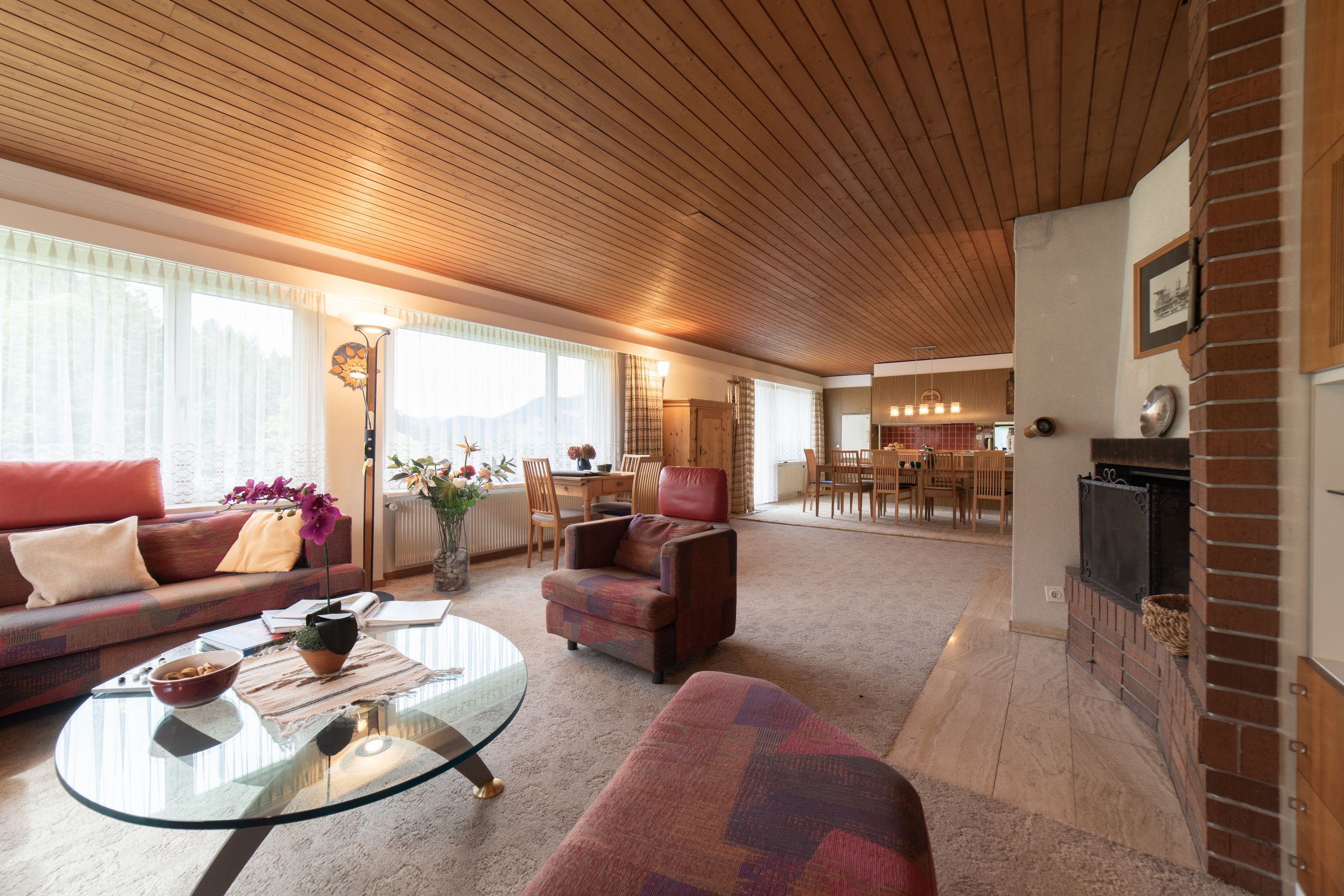 Un vaste salon doté d’un plafond en bois, d’une cheminée, d’un coin repas et d’un canapé offrant une vue sur l’extérieur.