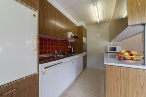 Una cocina compacta con armarios de madera, un refrigerador blanco, un microondas y un bol con fruta en la encimera.