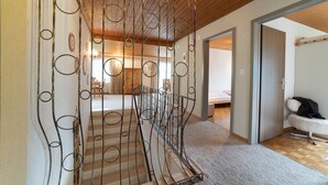 Una escalera con barandilla de metal decorada con diseños circulares, que conduce a una habitación con una cama y una silla blanca.