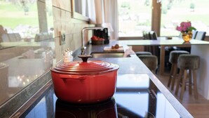 A modern kitchen with a red pot on an induction cooktop, a window with a view of greenery, and a dining area in the background. - Primula 4.5 room chalet next to the slopes (Wildhaus)