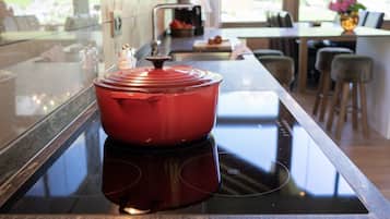 Une cuisine moderne avec une casserole rouge sur une plaque de cuisson à induction, une fenêtre donnant sur un paysage verdoyant et un coin repas à l’arrière-plan.