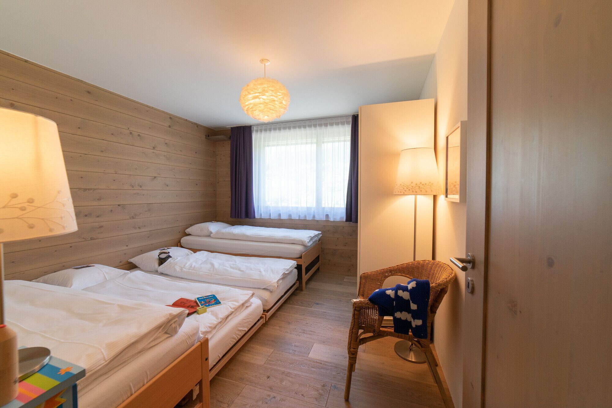 Una habitación con tres camas, una silla de mimbre y una lámpara.