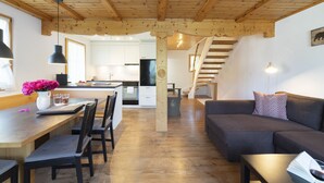 A spacious living area with a wooden ceiling, a dining table with chairs, a sofa, and a kitchen in the background.