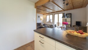 A kitchen with a wooden ceiling, a dining area with a table and chairs, and a TV on a stand.