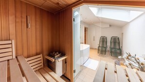A sauna room with wooden walls, a glass door leading to a bathroom, and a skylight.