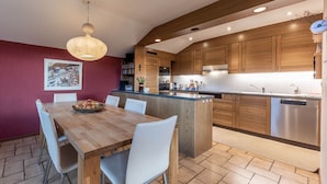 A modern kitchen with wooden cabinets, a central island, and a dining area with a wooden table and white chairs.