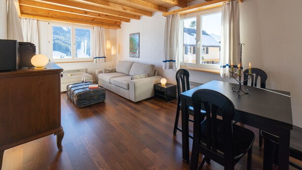 Una sala de estar acogedora con techo de madera, un sofá, una mesa con sillas y una ventana con vistas a montañas nevadas.