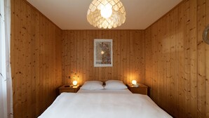 Habitación con paneles de madera, una cama, dos mesitas de noche con lámparas y una obra de arte enmarcada en la pared.