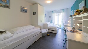Ein Schlafzimmer mit einem Einzelbett, einem Schreibtisch und einem Stuhl. An der Wand befinden sich Bilder und ein Fenster mit Vorhängen.
