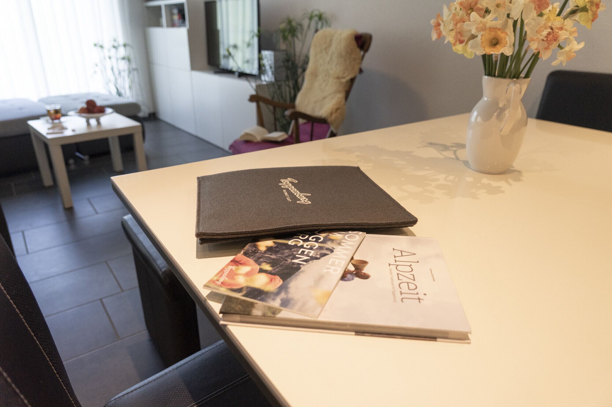Ett bord med en bärbar dator, en tidning och en vas med blommor.