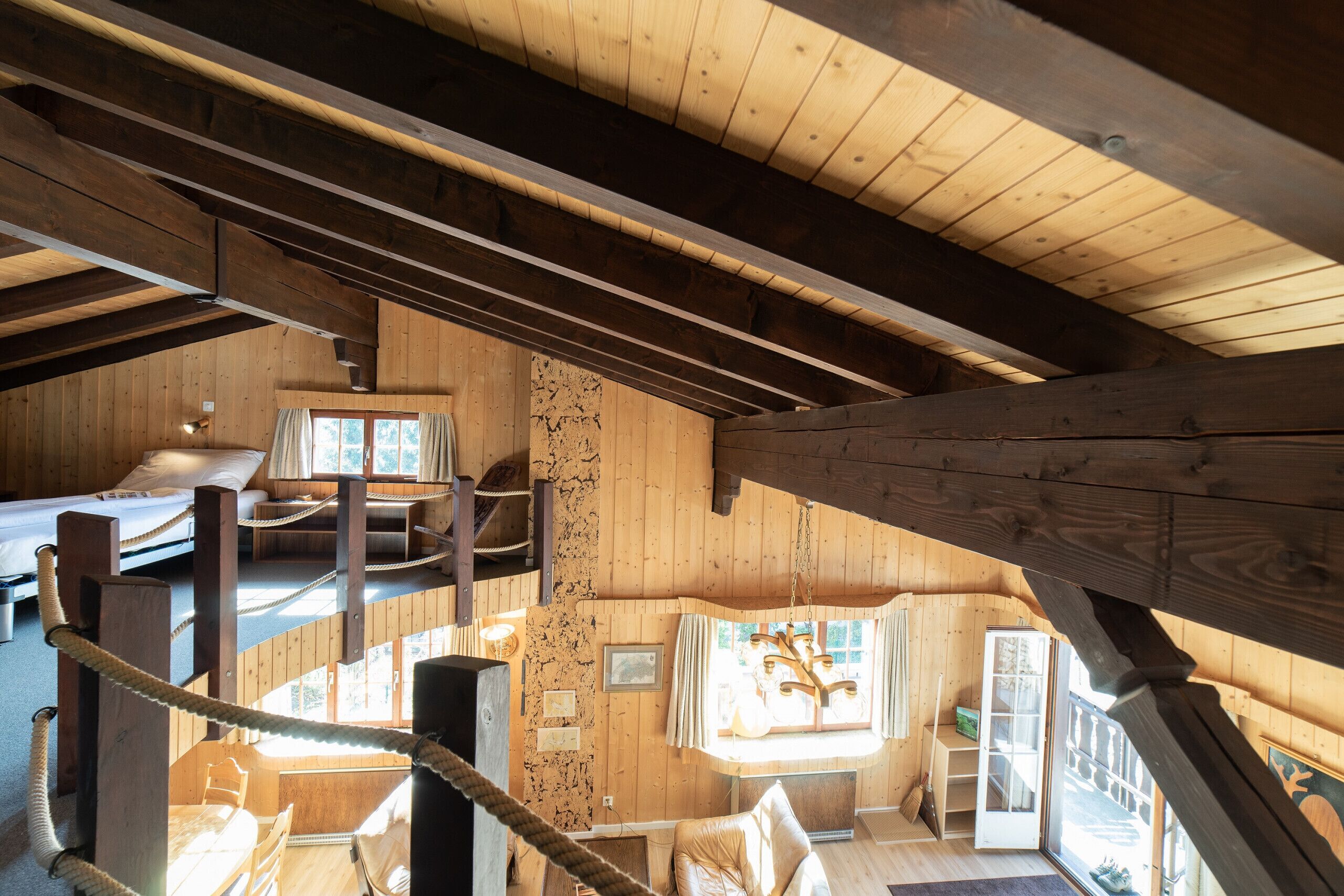 A wooden cabin interior with a loft bedroom, a dining area, and a kitchen.