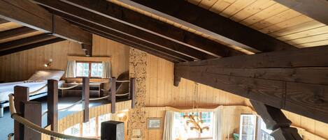 A wooden cabin interior with a loft bedroom, a dining area, and a kitchen.