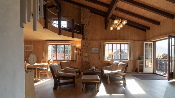 Un interior espacioso de madera con comedor, dos sillones de cuero, una mesita y una escalera a un nivel superior.
