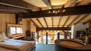 Interior de una cabaña de madera con una cama, un rincón de lectura, una mesita y una zona de estar circular.