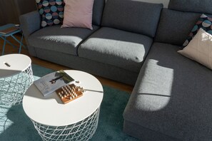 Ein graues Sofa mit einem gemusterten Kissen, ein runder weißer Couchtisch mit einem Buch und einem Holzspiel, und ein blauer Sessel.