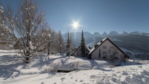 A snow-covered landscape with a house and mountains in the background.
