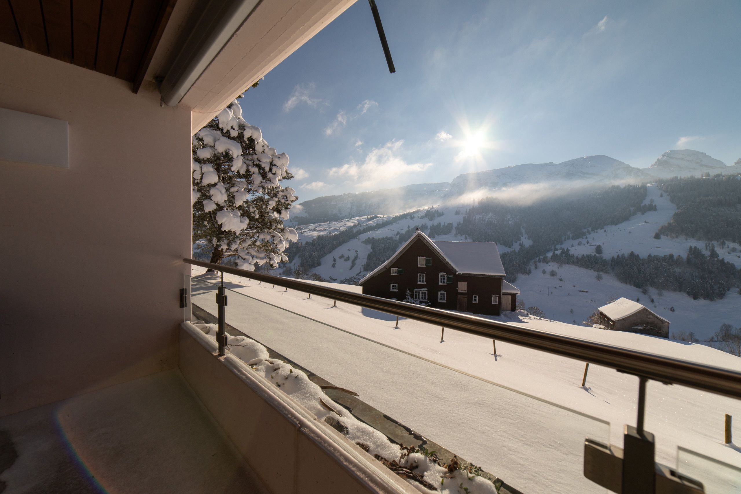 A balcony with a view of a snow-covered landscape, a wooden building, and a clear sky.