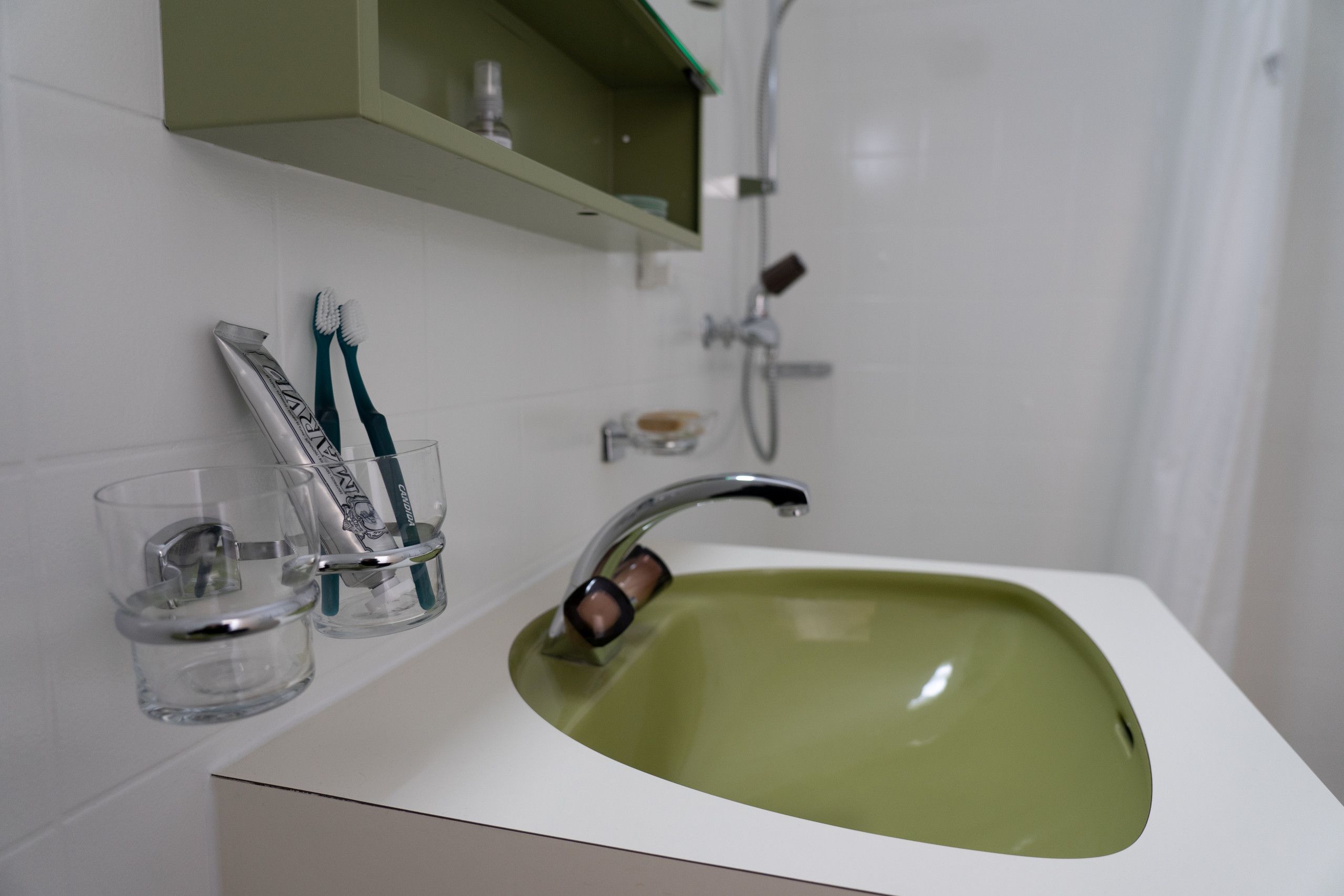 Ein Badezimmer mit Waschbecken in Weiß, einer grünen Schüssel und zwei Zahnbürsten in einem Glasbehälter.