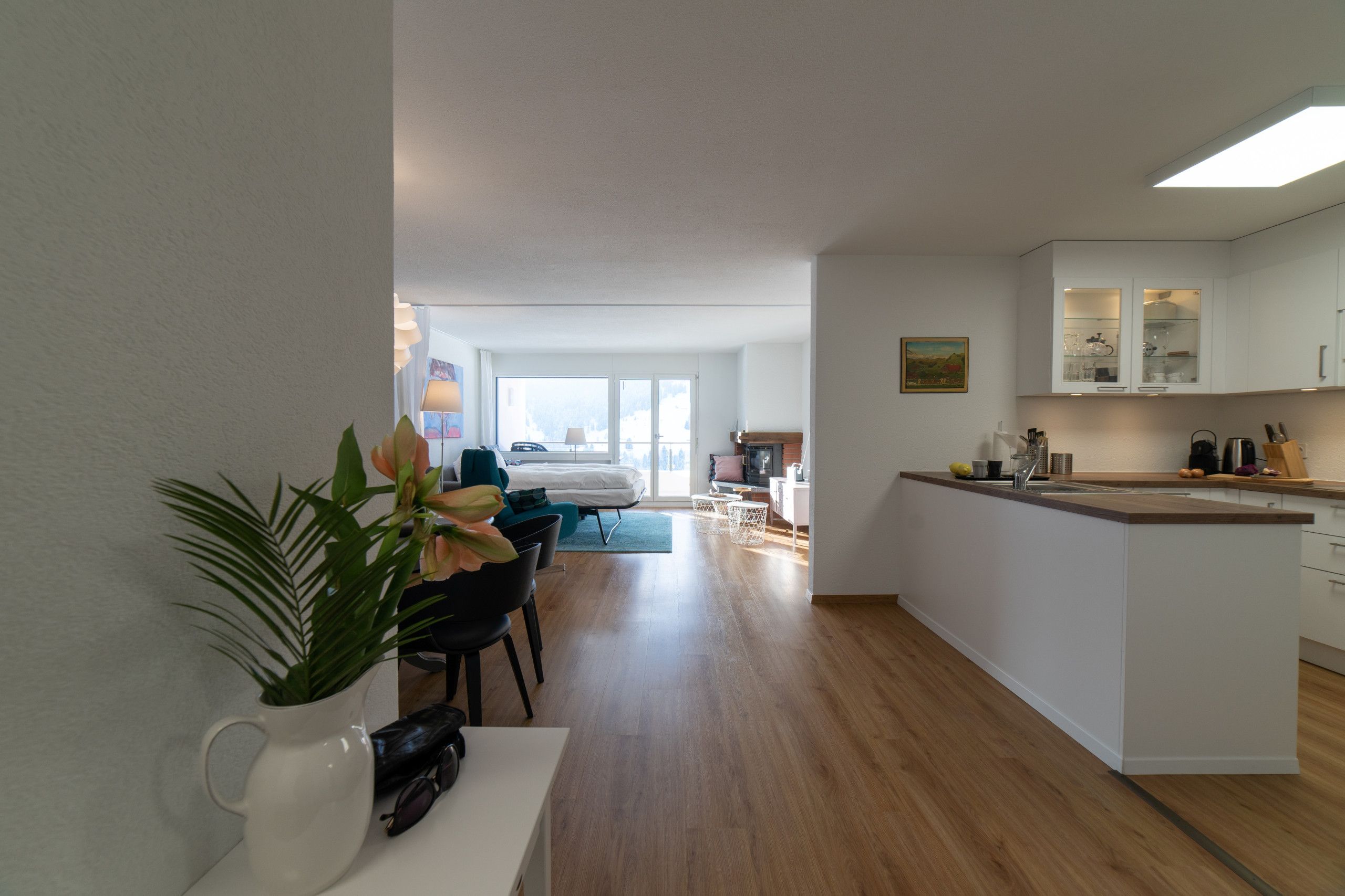 A modern kitchen with white cabinetry, a dining area with a table and chairs, and a view of a bedroom through an open door.