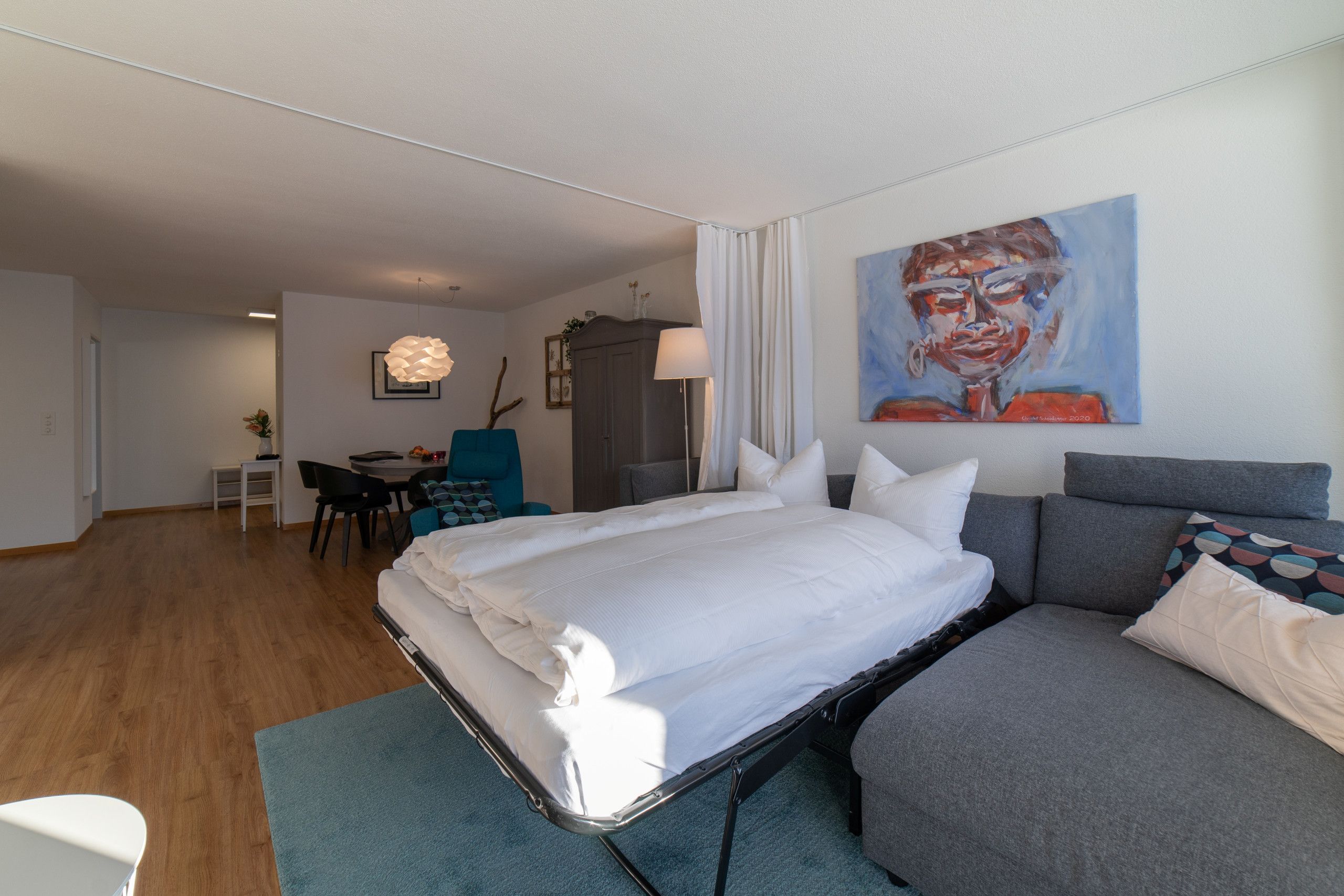 Moderni hotellihuone, jossa on sänky, sohva, työpöytä ja taulu seinällä.