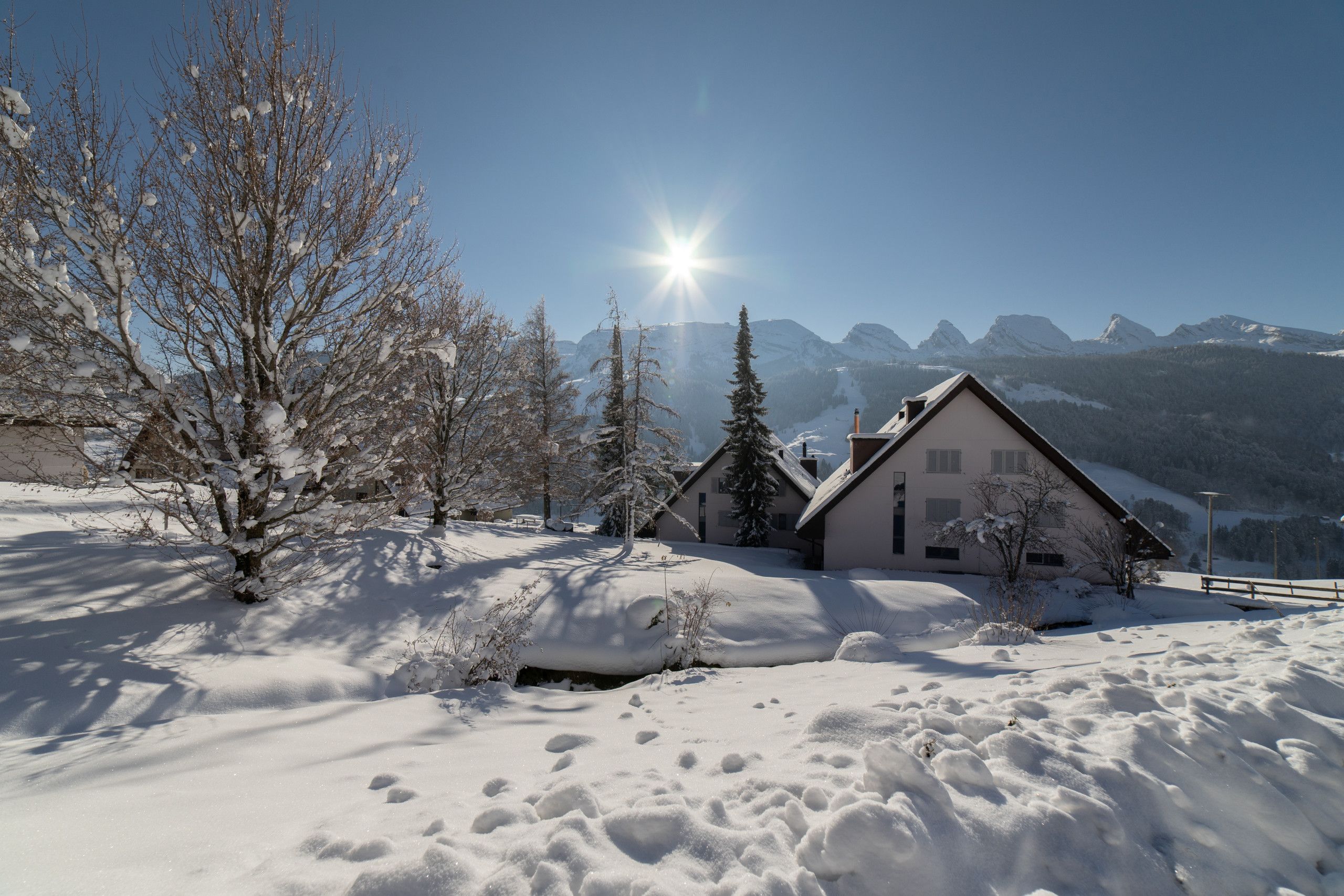 A snow-covered landscape with a house and mountains in the background.
