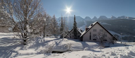 Een besneeerd landschap met een huis en bergen op de achtergrond.