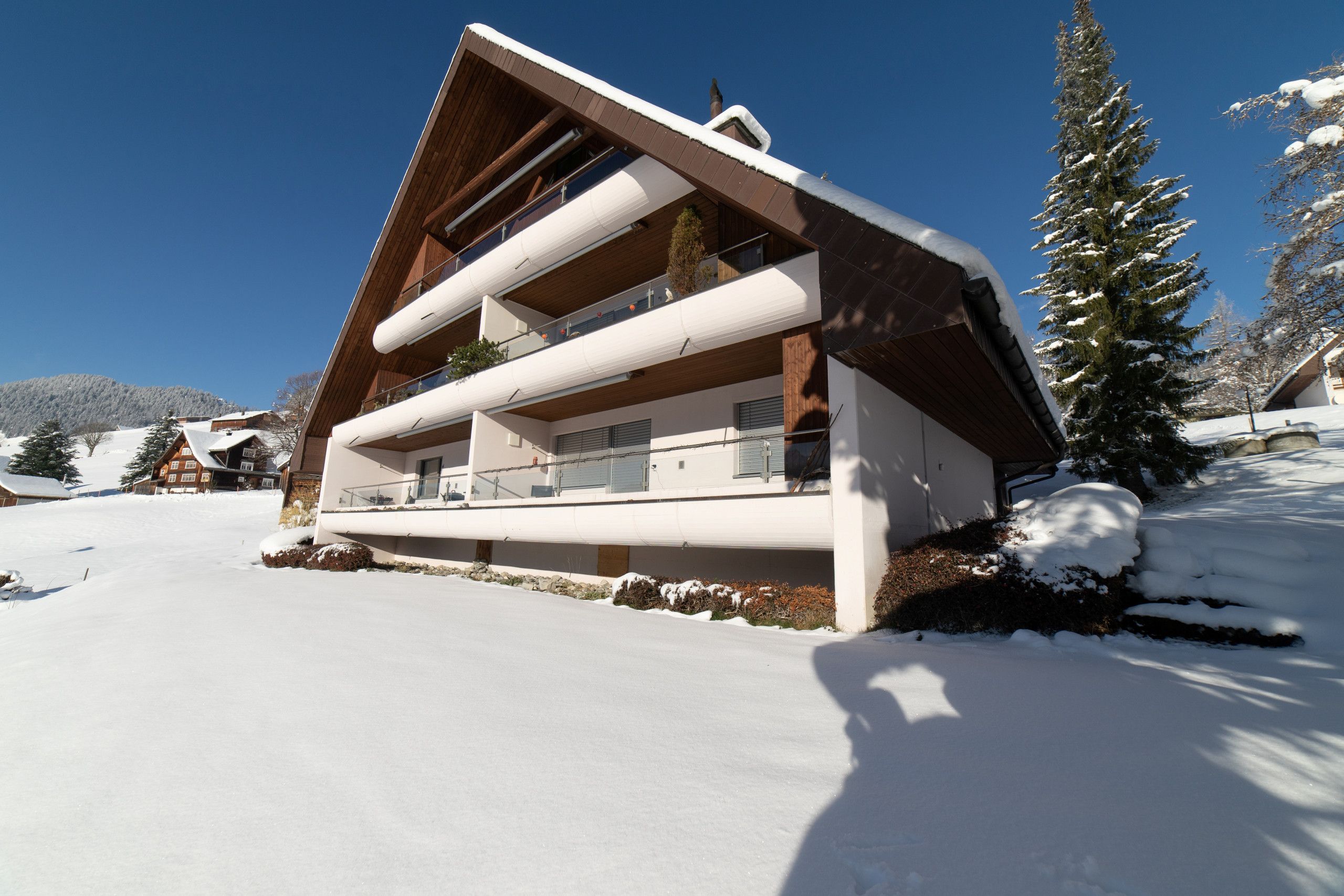 Verschneites Haus mit Balkonen in sonniger Winterlandschaft