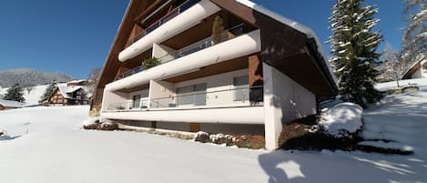 Verschneites Haus mit Balkonen in sonniger Winterlandschaft