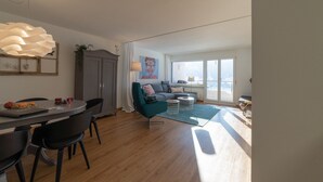 A modern living room with a sofa, a dining table with chairs, and a large window with a view.