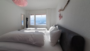 A bedroom with a large bed, a window with a view of a snowy landscape, and a hanging plant.