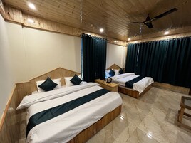 A hotel room with two beds, wooden headboards, a wooden floor, a ceiling fan, and a nightstand with a kettle.