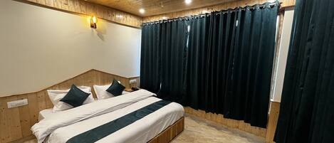 Ein Schlafzimmer mit einem Holz-Kopfteil, einem Bett mit weißer und grüner Bettwäsche, einem Deckenventilator und dunklen Vorhängen.