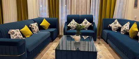 Una sala de estar con dos sofás azules, una mesa de centro de vidrio y cojines estampados.