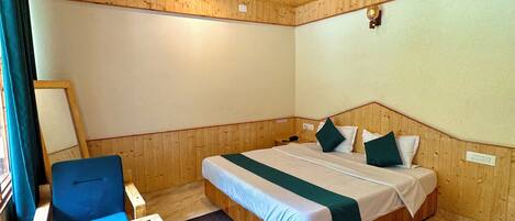 A room with a wooden ceiling, a bed with a green and white bedspread, a blue chair, and a small table.