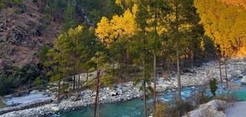 A mountainous landscape with a river, trees, and a suspension bridge.