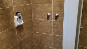 Eine kleine, mit Fliesen ausgekleidete Duschkabine mit einer Handseifenspender und zwei Wasserhähnen.